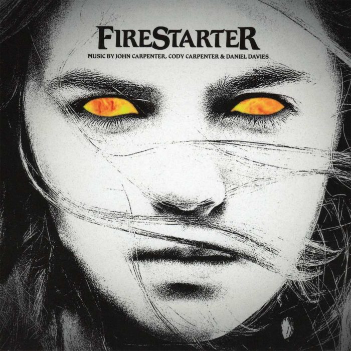 CD cover for the "Firestarter" soundtrack. The cover features a close-up of a woman's face with glowing yellow eyes, a stark black and white aesthetic, and the title "Firestarter" along with the names of the composers John Carpenter, Cody Carpenter, and Daniel Davies.