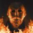 A close-up of Michael Myers' iconic mask, engulfed in flames. The mask is distorted and charred, with glowing eyes that appear menacing. The image is dark and intense, suggesting danger and evil.